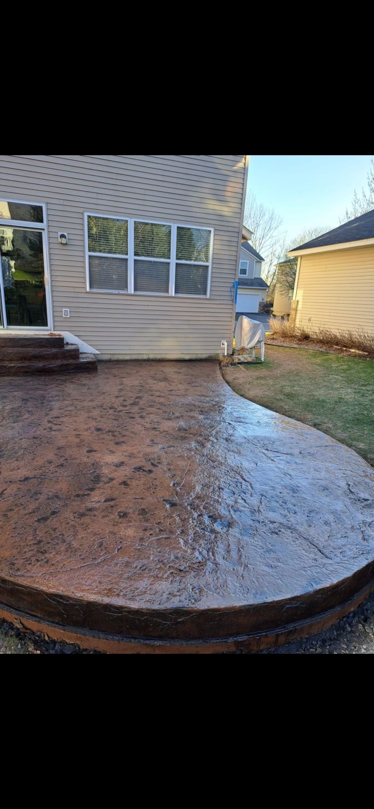 A newly poured concrete patio in a backyard setting.