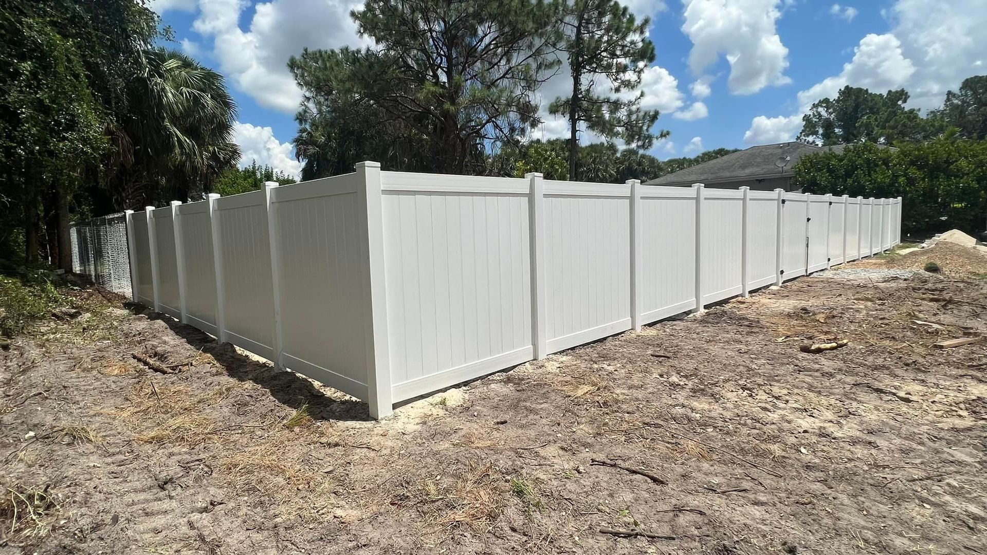 White vinyl fence in a yard under a blue sky with some trees.