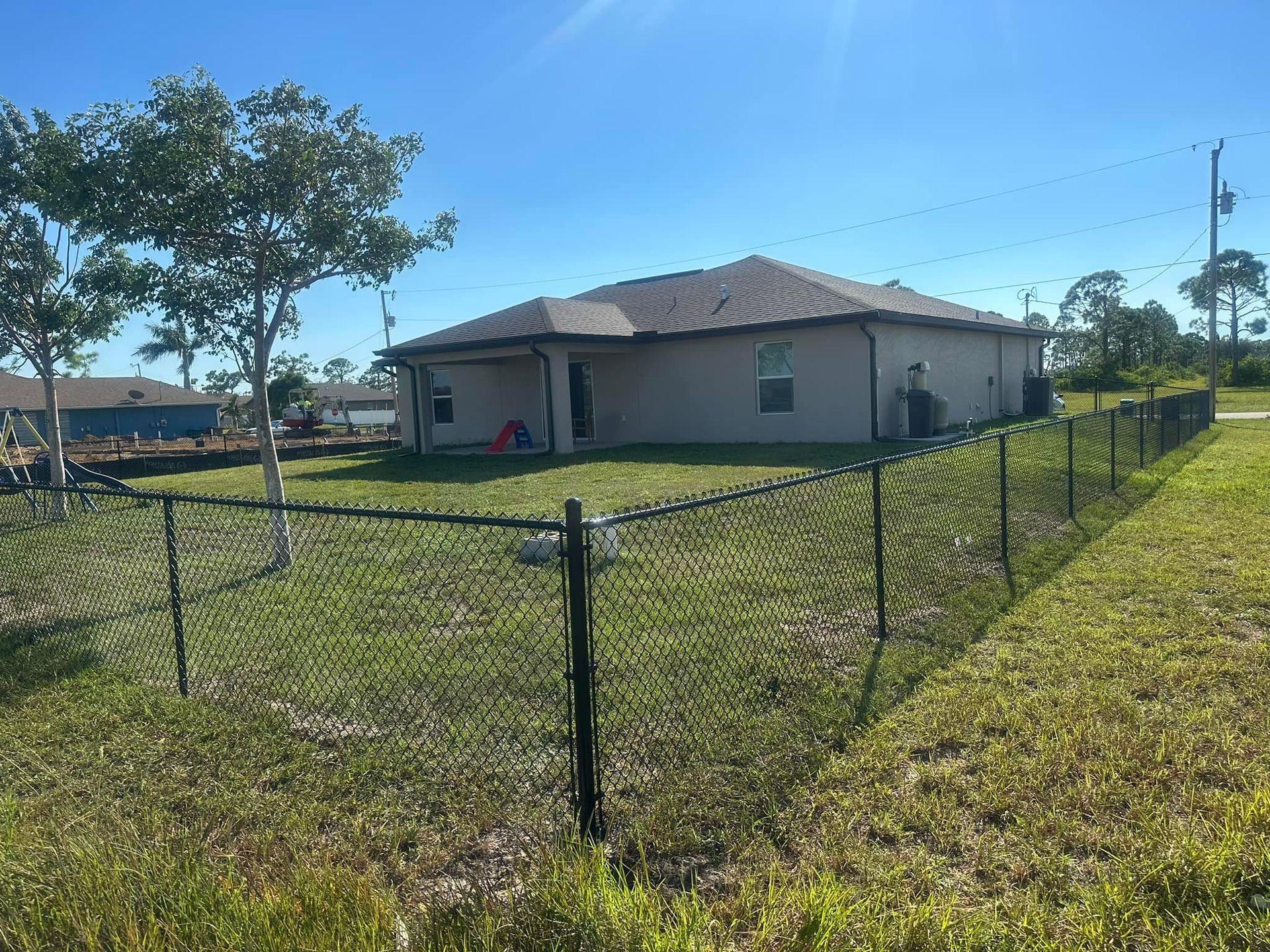 A house with a black chain-link fence in a grassy yard under a clear blue sky.
