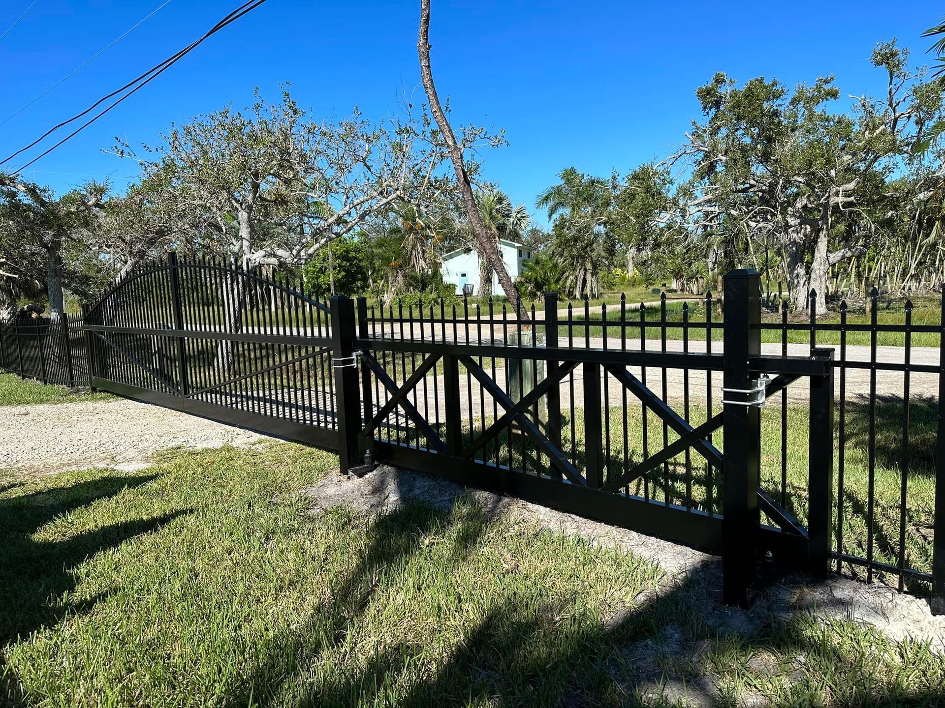 Black metal gate and fence on a grassy lawn, under a clear blue sky.