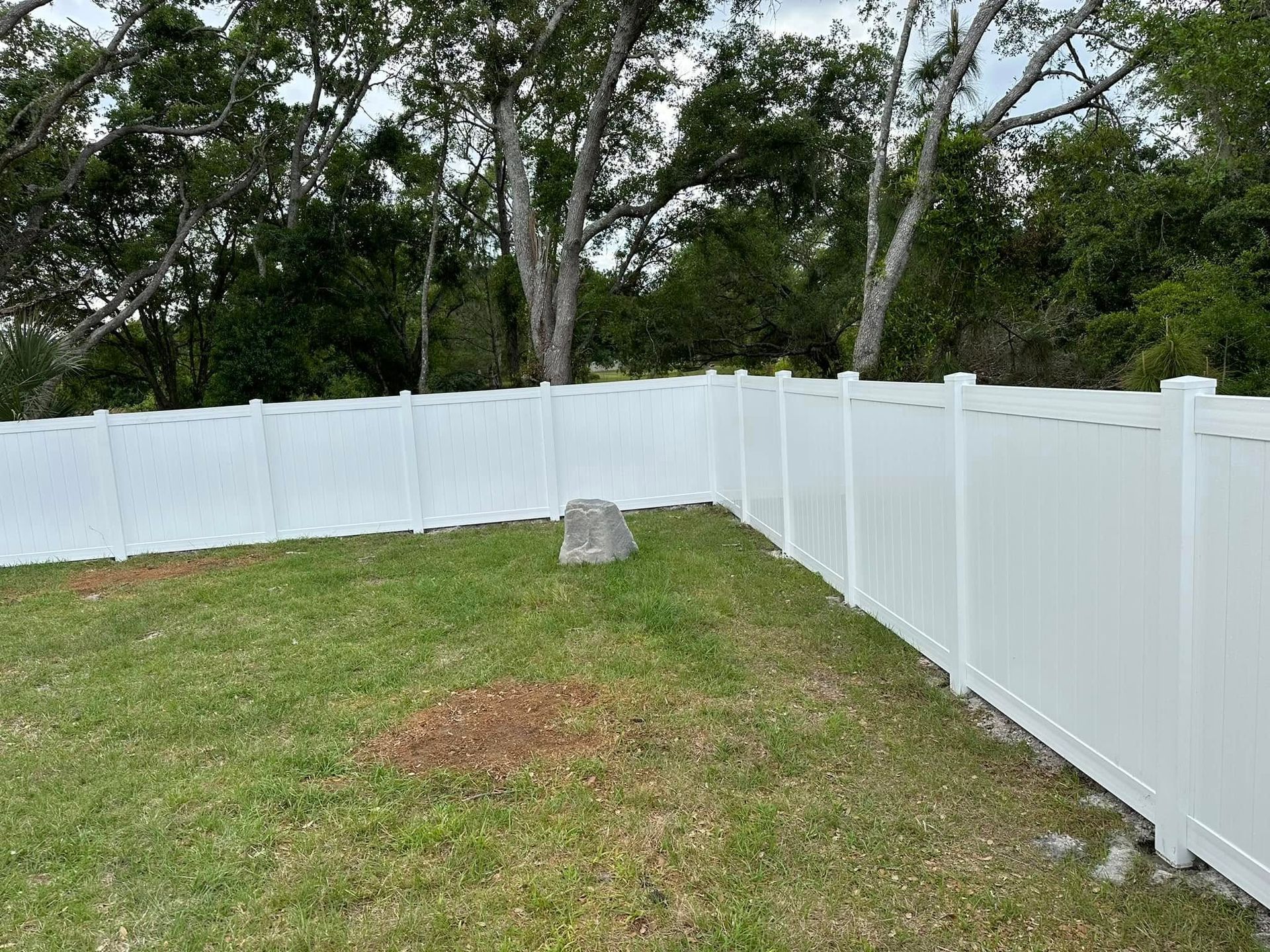 White vinyl fence surrounds a grassy yard, trees in the background.