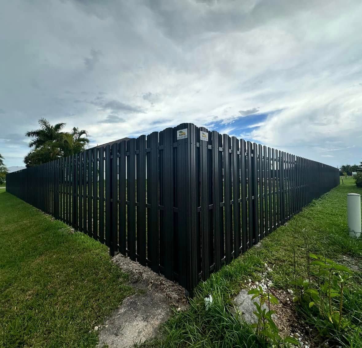 Black fence, corner view. Green grass, cloudy sky.