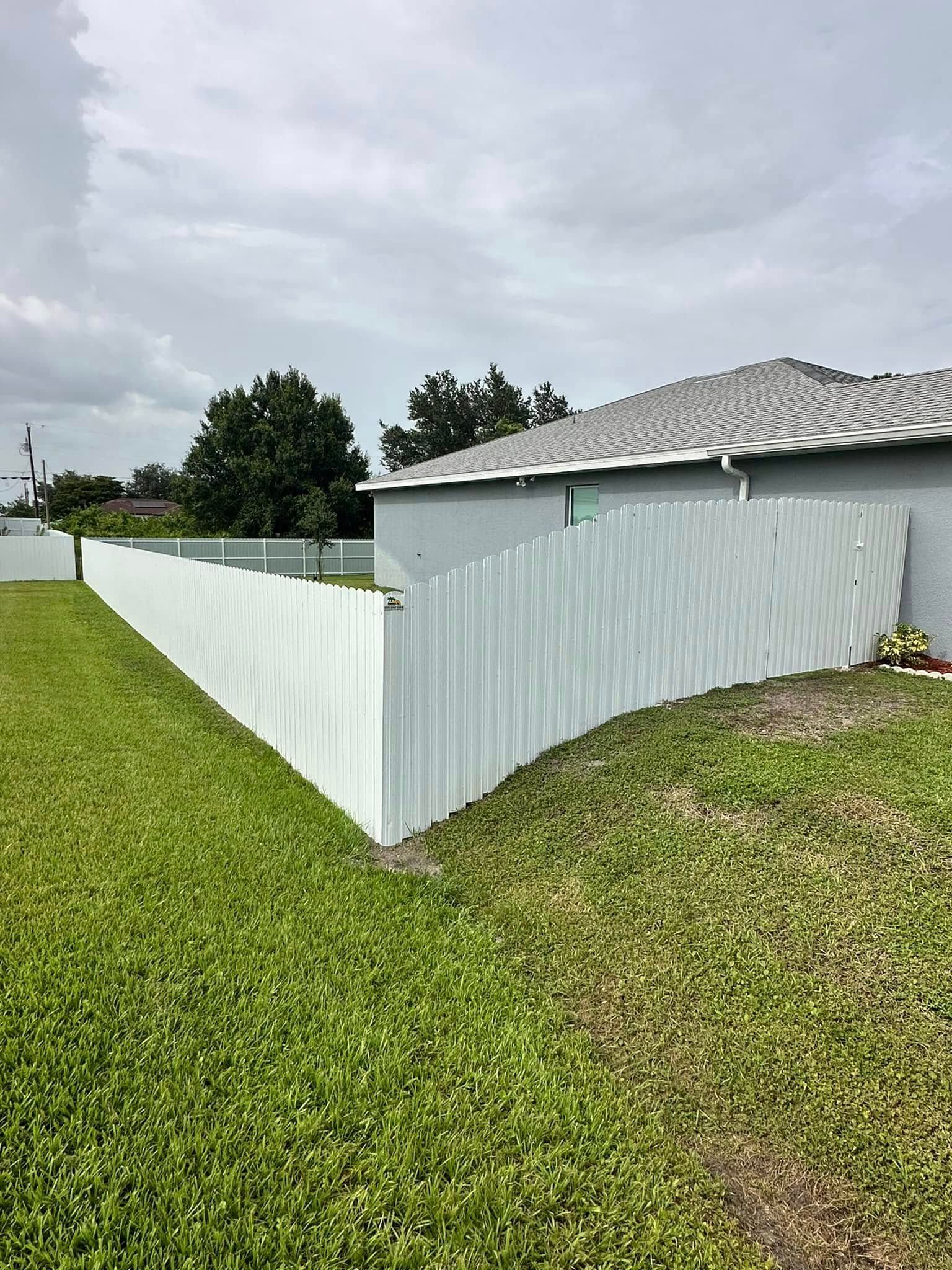 White picket fence bordering green grass and a light gray house under a cloudy sky.