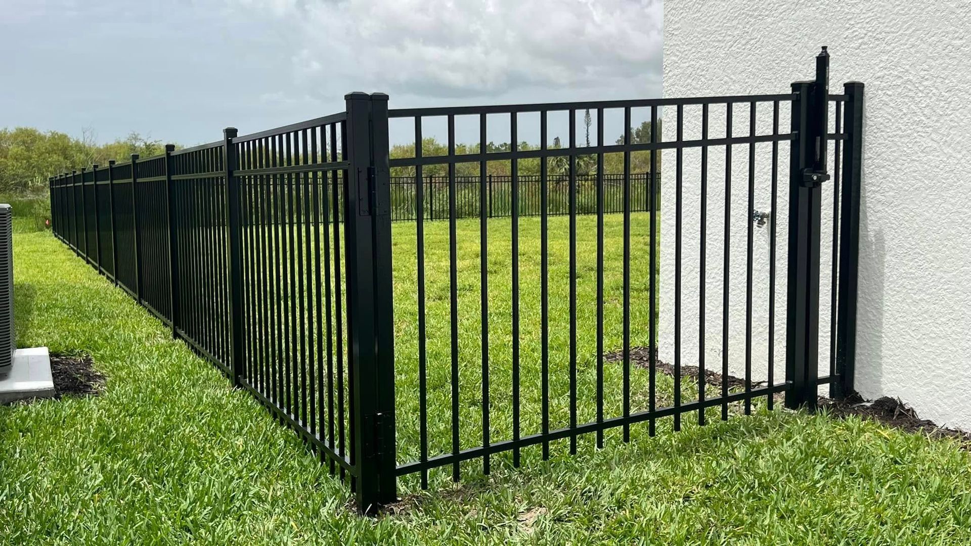 Black metal fence encloses a grassy yard, adjacent to a white building.