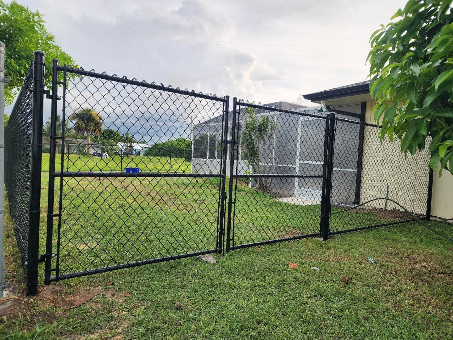Black chain-link fence with double gate in a yard, a house visible in the background.