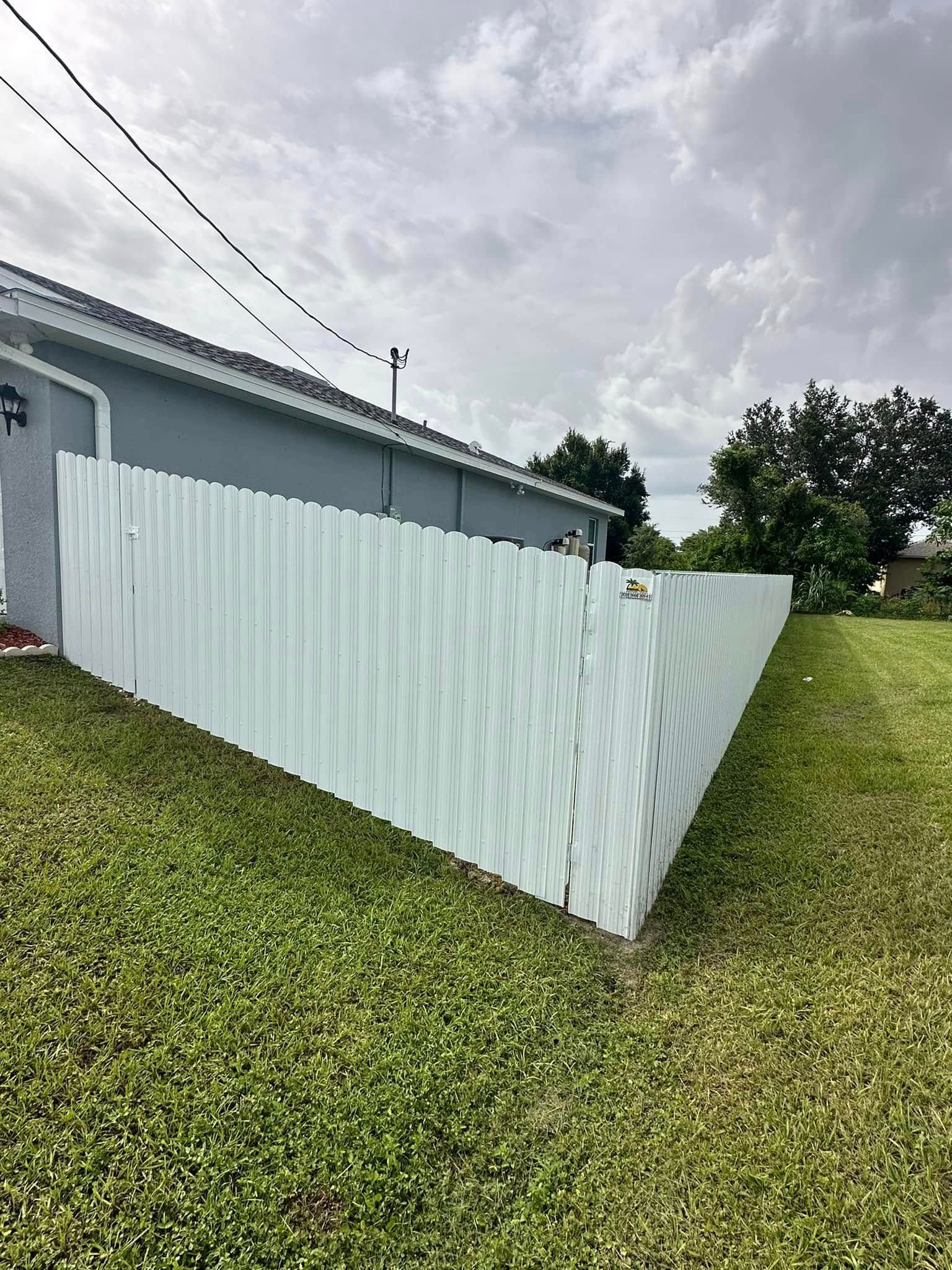 White fence surrounding a grassy backyard next to a house under an overcast sky.