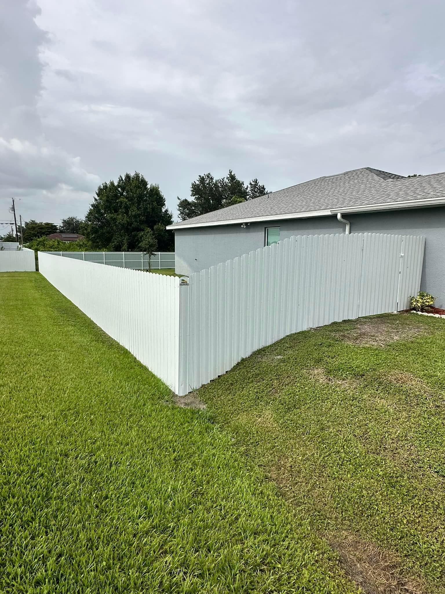 White picket fence bordering a grassy yard, next to a gray house under an overcast sky.