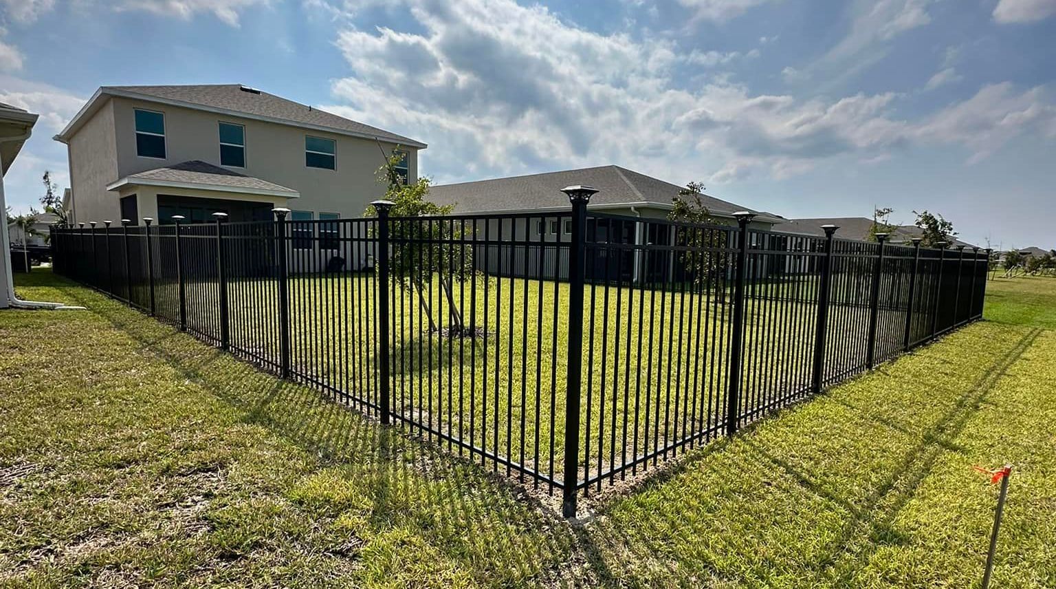 A black aluminum fence surrounds a lush green field.