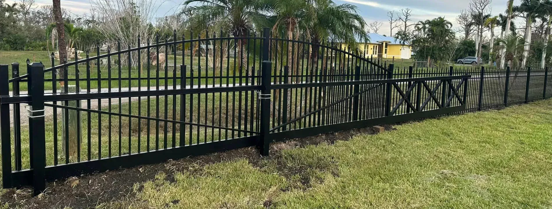 A black aluminum fence surrounds a lush green field.