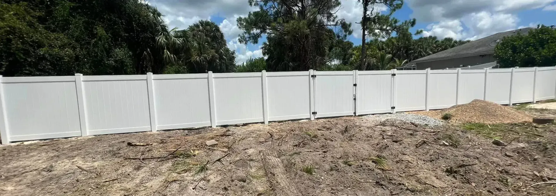 A white vinyl fence is sitting in the middle of a dirt field.
