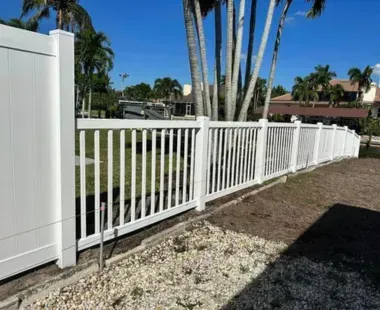 A white fence with palm trees in the background