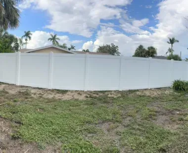 A white fence surrounds a grassy field in front of a house.
