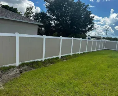 A white and tan vinyl fence is in the backyard of a house.