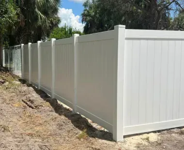 A white vinyl fence is sitting on top of a dirt field.