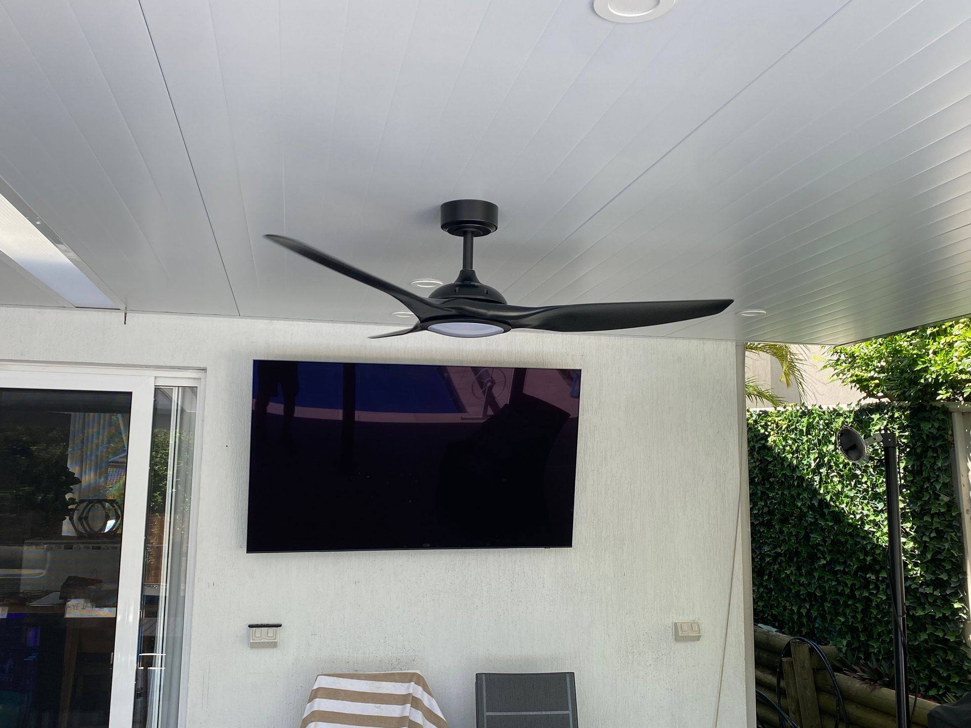 A black ceiling fan hangs above a large, wall-mounted television — Channel Electrical In Swansea Heads, NSW