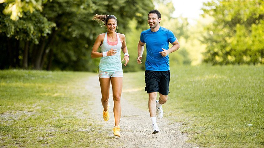 Two runners jogging on a grassy park trail on a sunny day
