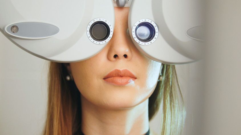 Person using a dual-lens eye testing device, facing forward with a neutral expression.