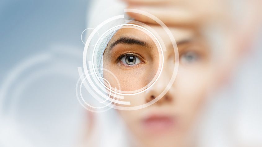 Close-up of a face with an eye centered in a circular interface overlay, hand blurred in foreground
