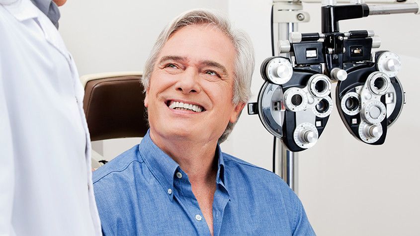 Smiling patient seated for an eye exam beside a phoropter in a bright clinic
