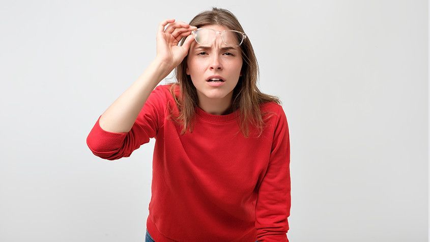 Woman in a red sweater touching her forehead with a concerned expression against a plain background