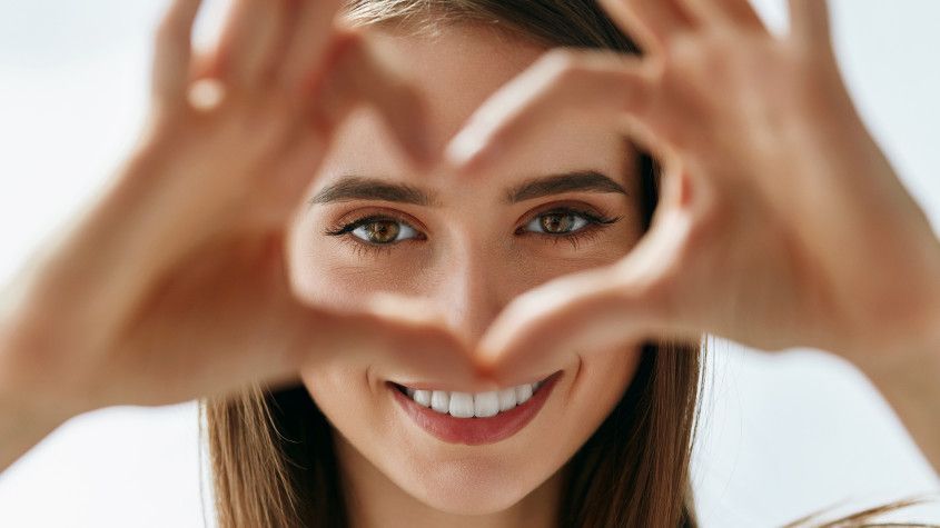 Smiling woman framing her face with hands in a heart shape
