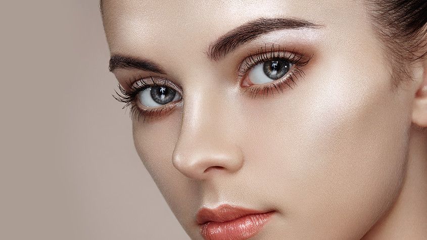 Close-up of a woman’s face with blue eyes, neutral makeup, and a soft beige background