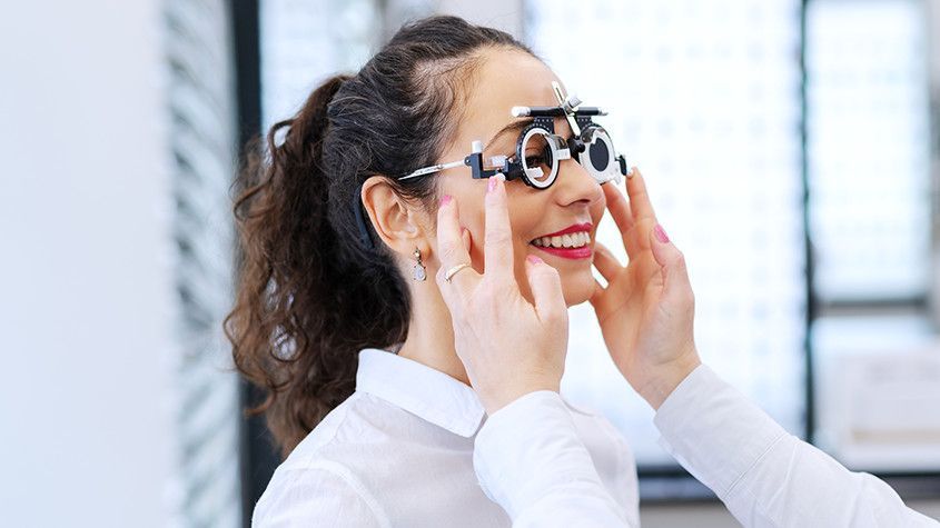 Person adjusting trial eyeglasses while smiling in an optometry office