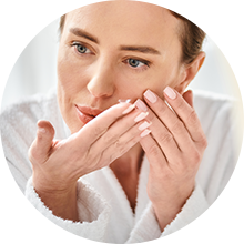 Woman applying cream to her face in a white robe