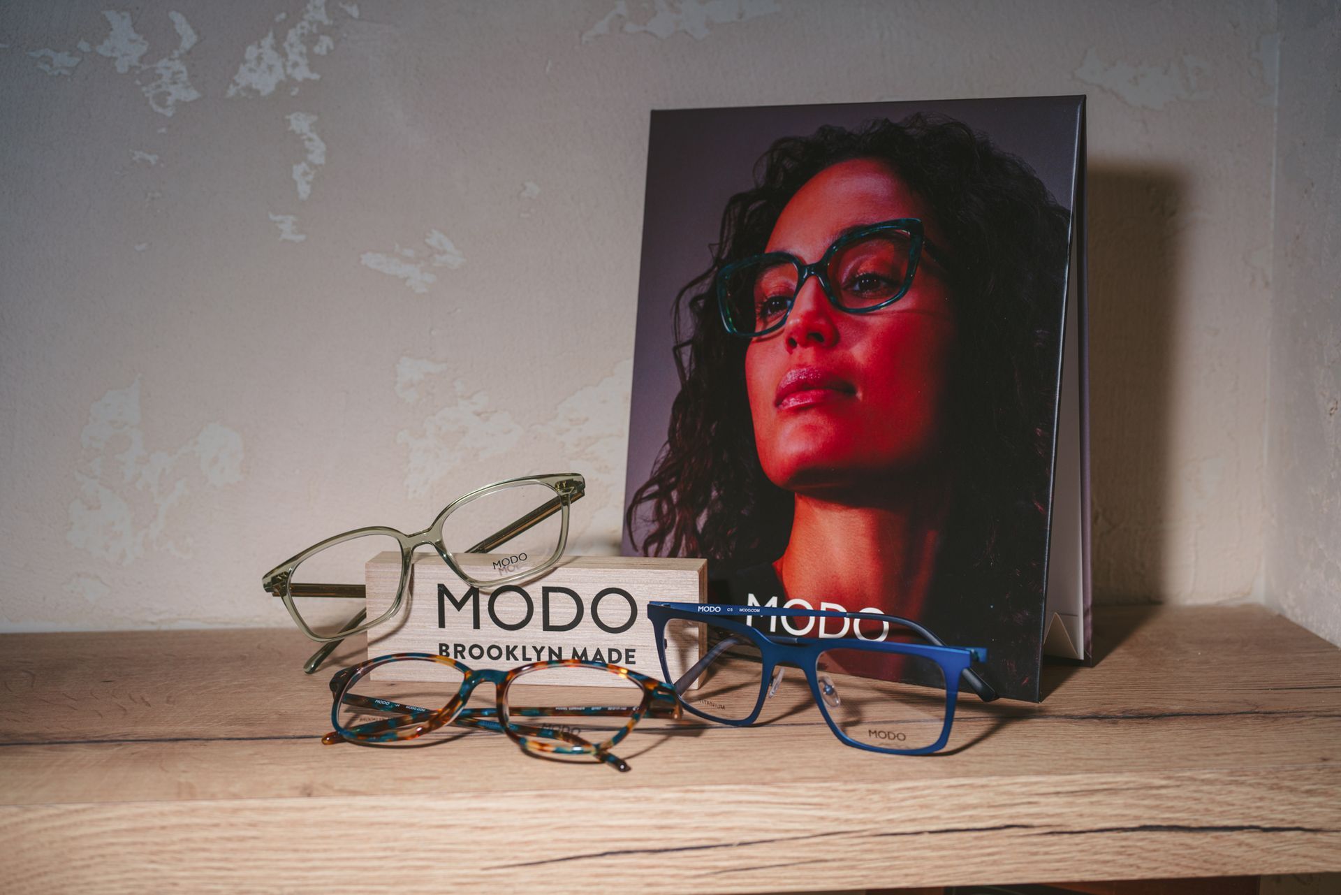 Eyeglasses displayed in front of a portrait print leaning against a wall on a wooden surface.