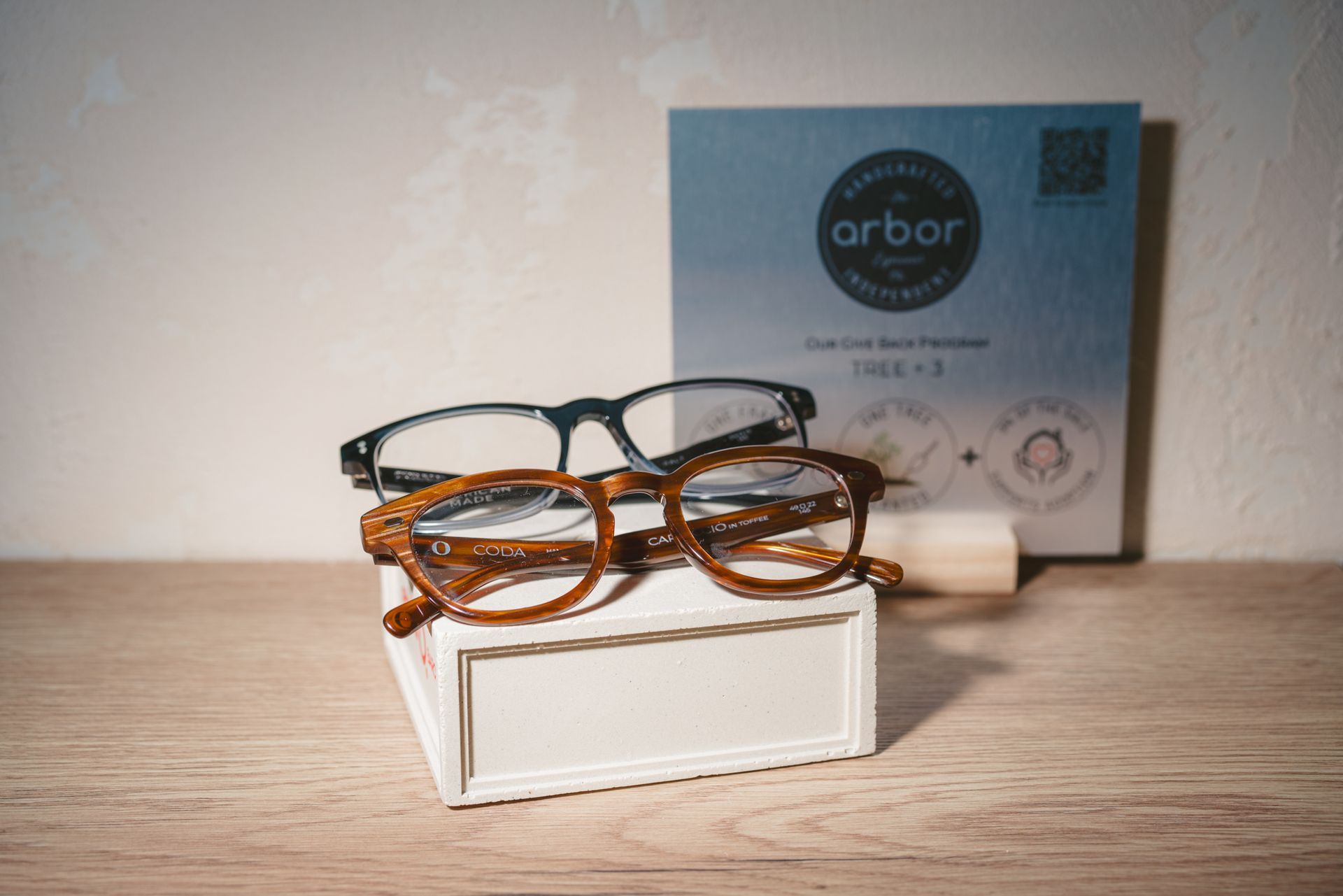 Two pairs of eyeglasses on a white box with an Arbor product package in the background