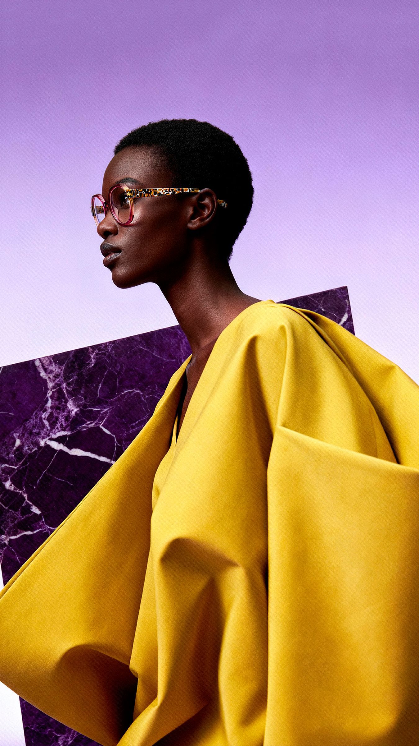 Person in oversized yellow garment against a purple sky and rocky backdrop.