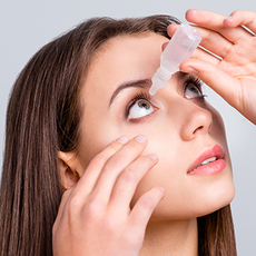 Woman applying eye drops to her eye with a bottle and hand, close-up on a white background