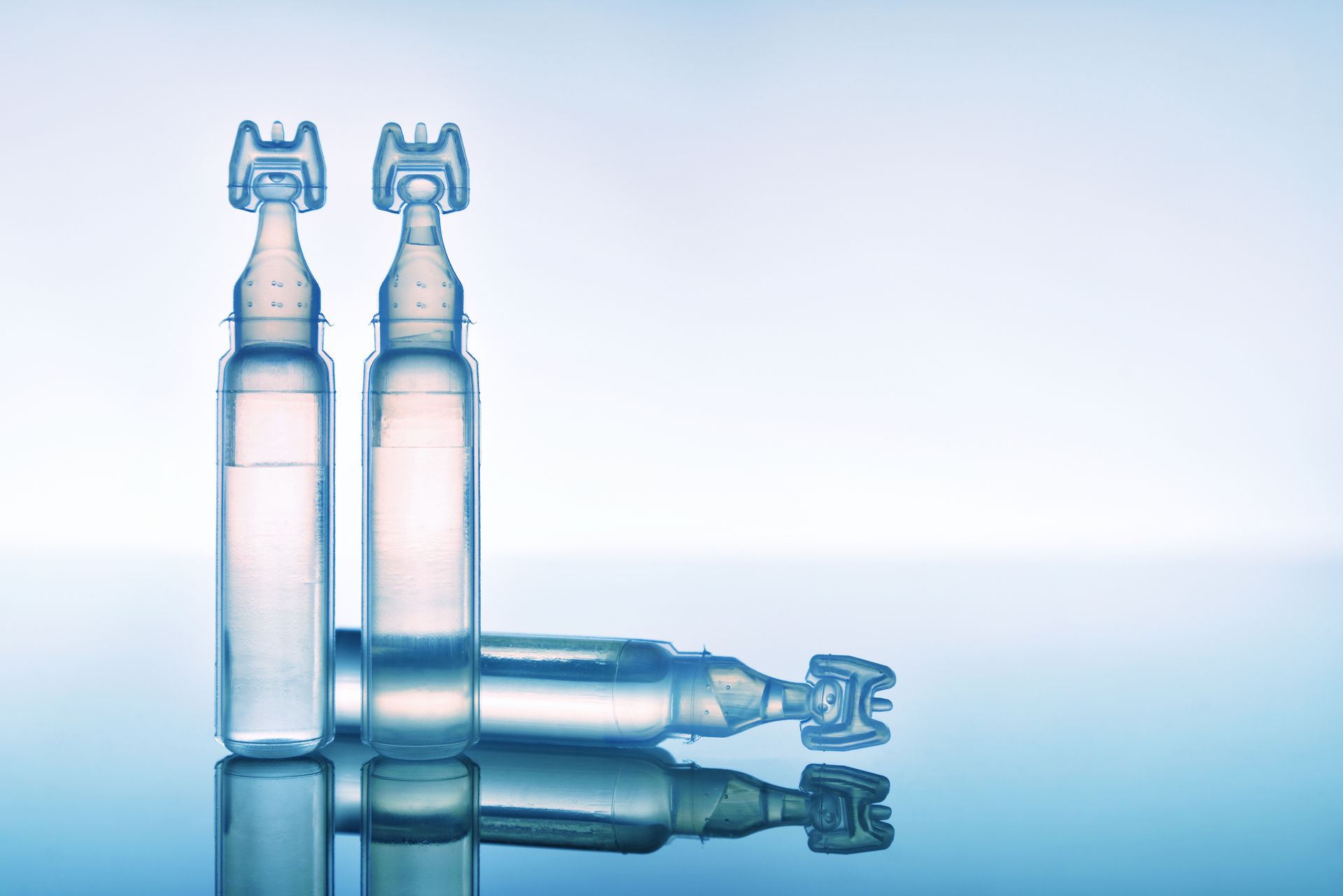 Two clear glass bottles standing and lying on a reflective blue surface against a pale background