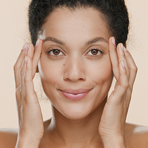 Smiling person gently touching their face against a soft beige background
