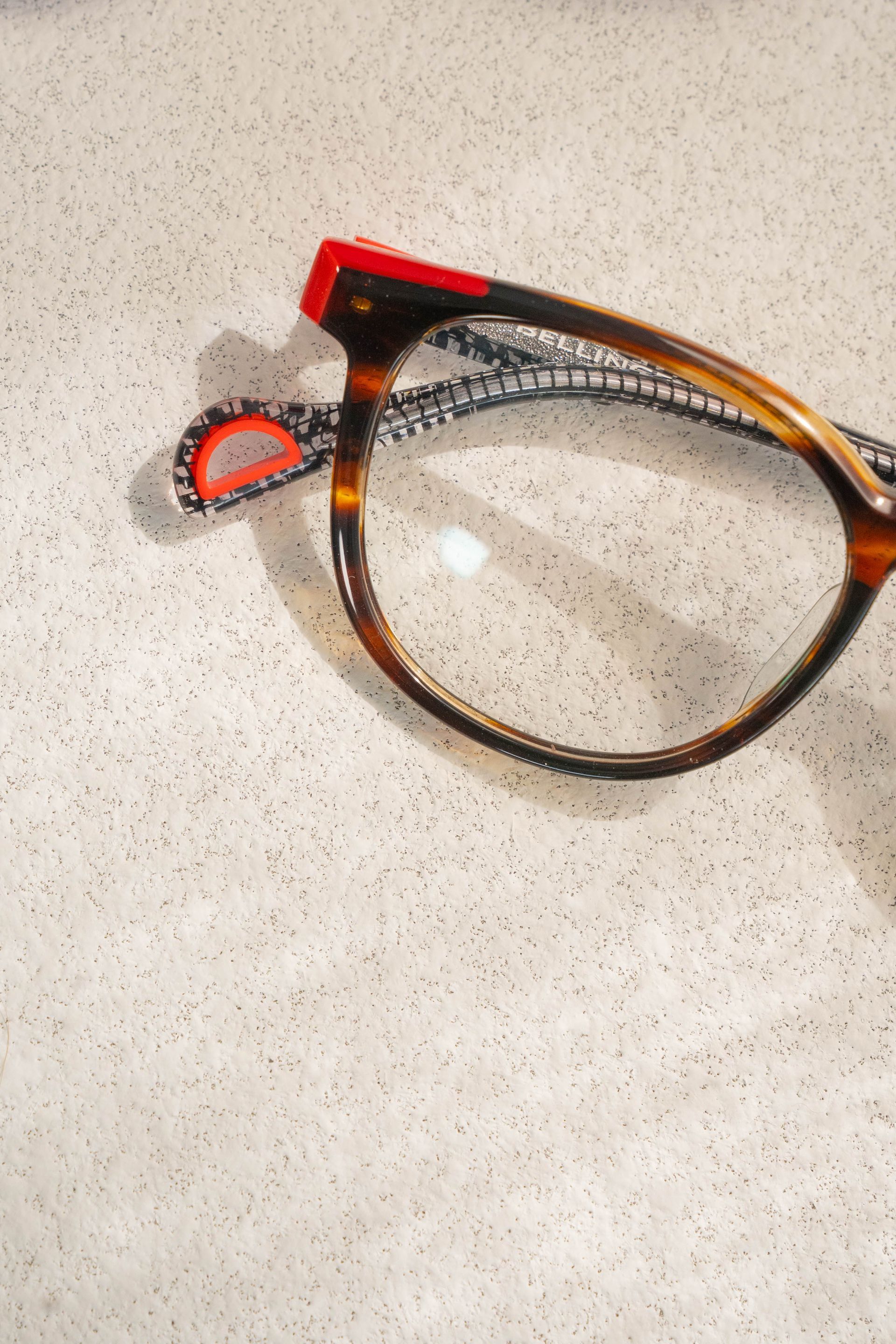 Tortoiseshell eyeglasses with a red temple hinge on a speckled countertop