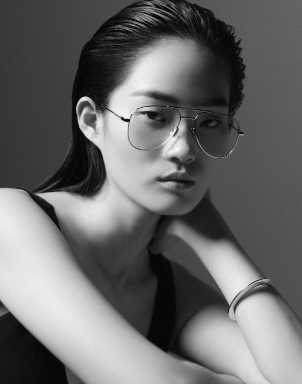 Portrait of a person with glasses, resting their chin on a hand, in a black-and-white studio setting