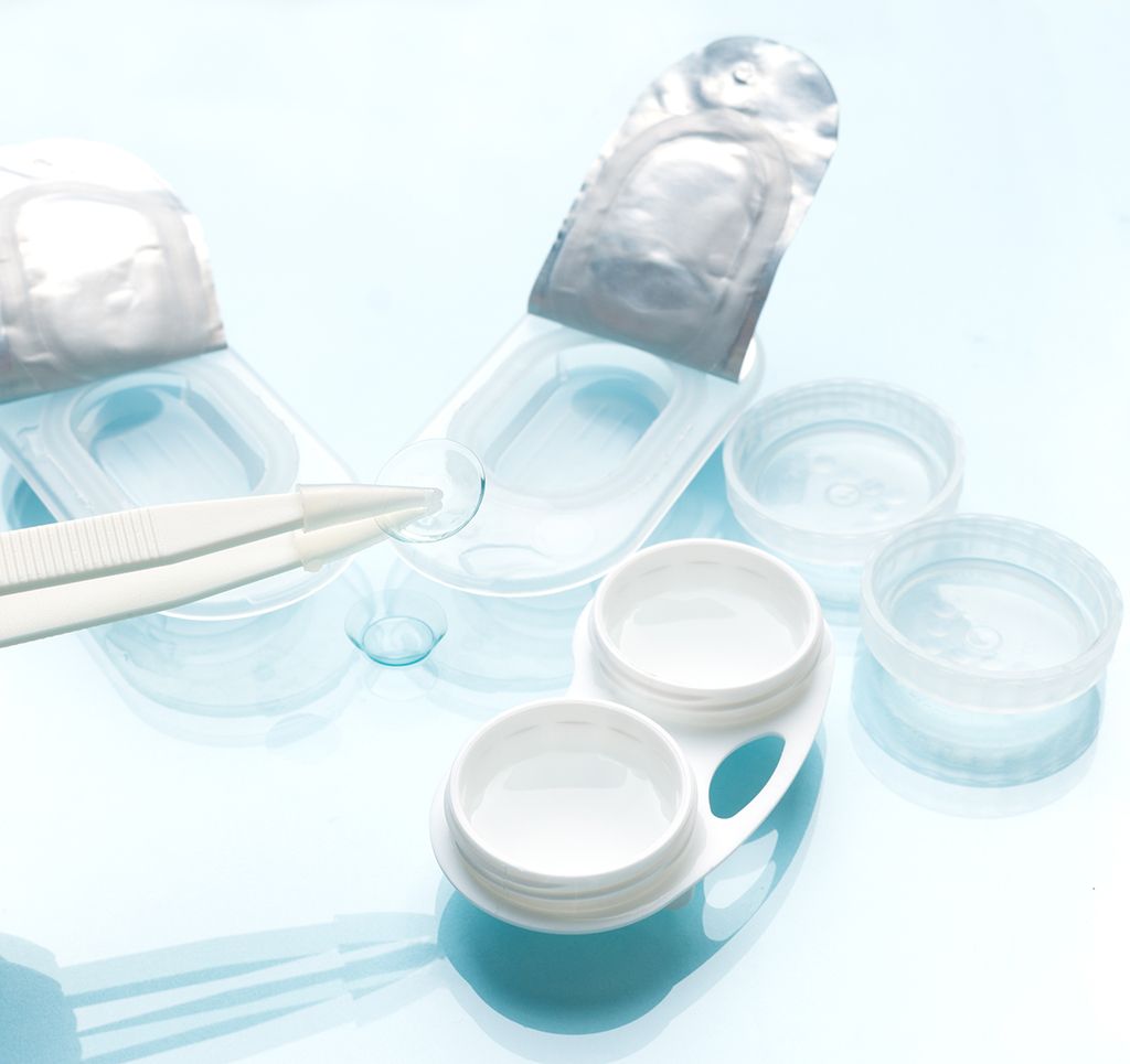 Blue and white contact lens cases and lenses on a light background, with tweezers nearby