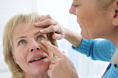 Person examining another person's eye with hands, in a bright clinical setting