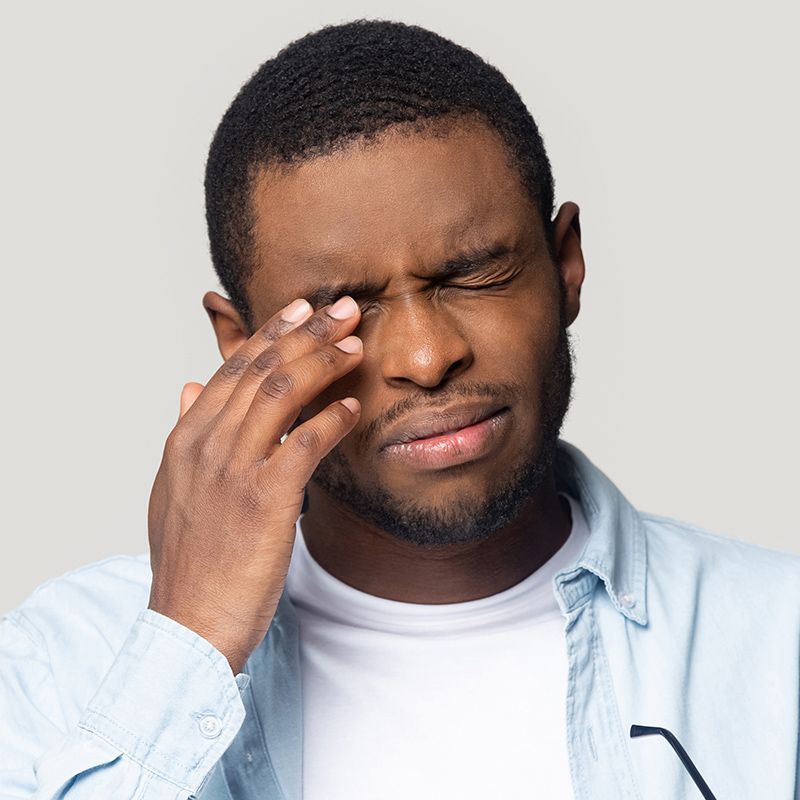 Man rubbing his eye with a pained expression against a plain background