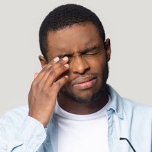 Man rubbing his eye with a pained expression against a plain background