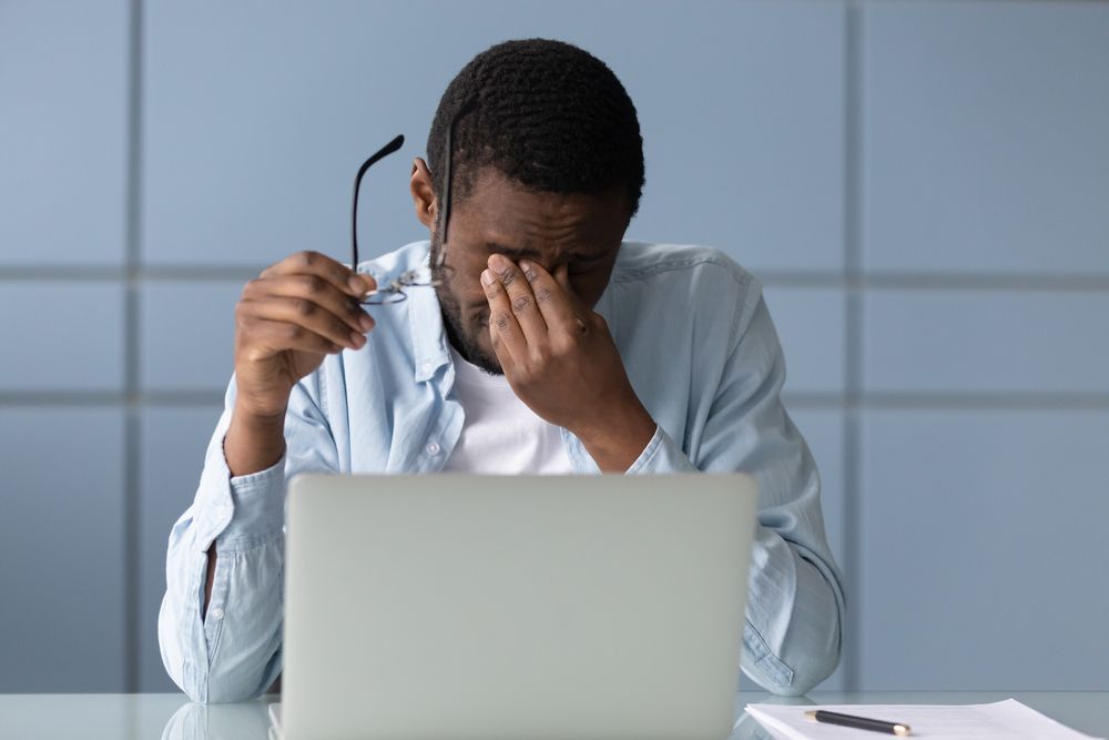 man with dry eyes rubbing his eyes working at computer desk