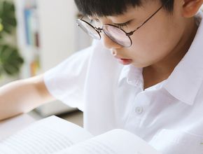 Child in glasses reading a book in a bright classroom
