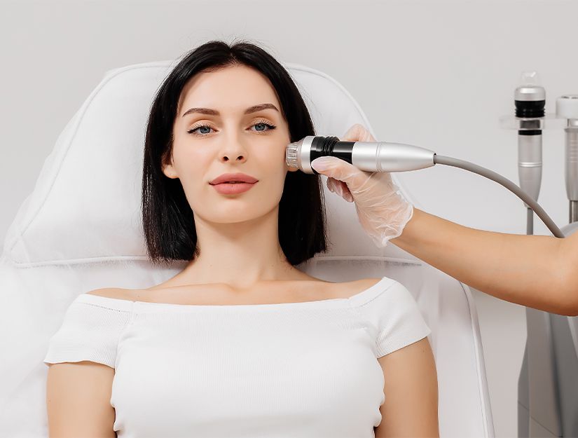 Woman receiving a facial treatment with a handheld device in a bright spa setting