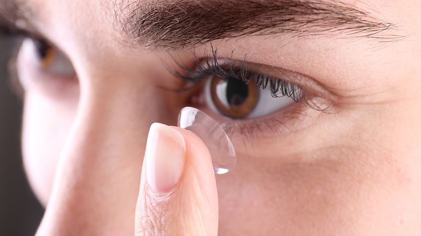 Close-up of a person inserting a contact lens into an eye
