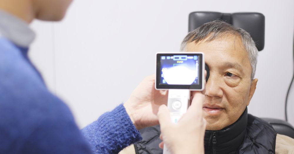 Person using a handheld device to photograph an older man during an eye exam