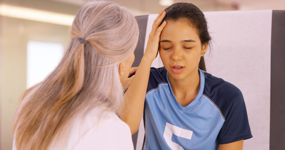 Woman comforting a soccer player with hand on her forehead in a bright indoor setting