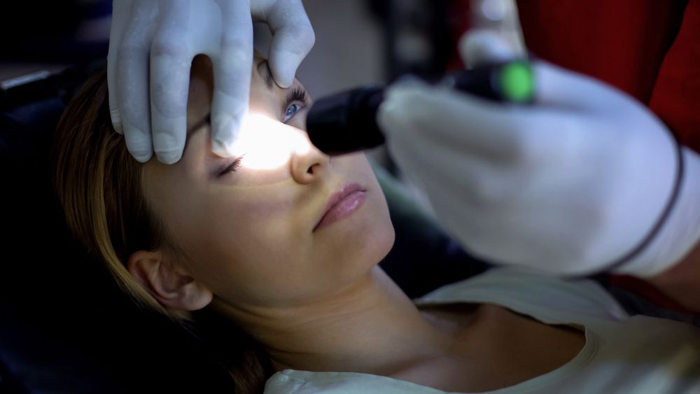 Dentist examining a patient’s eye with a bright light, close-up in a clinical setting