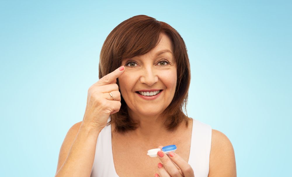 Smiling woman applying eye cream, holding a tube against a light blue background