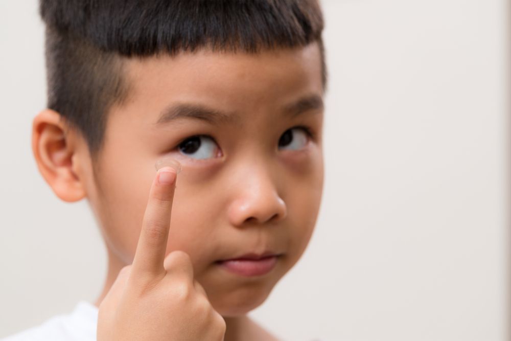 Child pointing to eye with finger, looking upward against a plain background