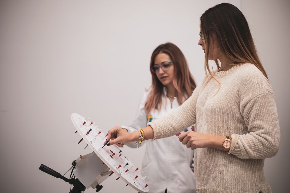 Two women reviewing a display board, one pointing at notes on a music stand in a bright room